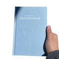 Light blue 'church journal' held by a hand on a white background