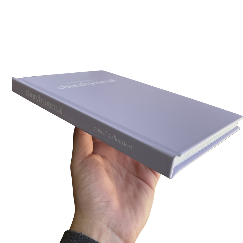 Hand holding a light purple journal with 'church journal' branding on a white background