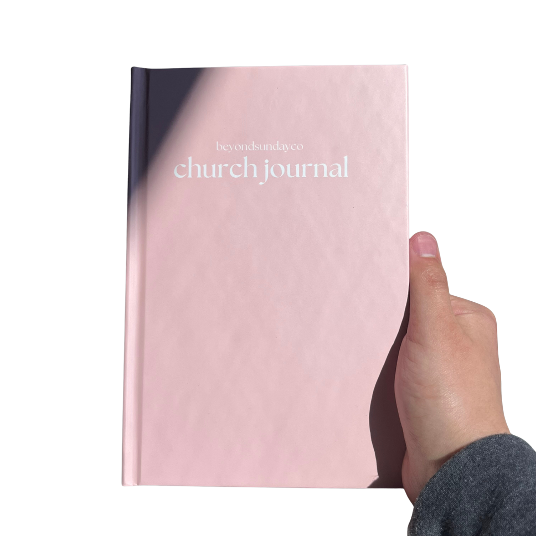 Pink 'church journal' held by a hand on a white background