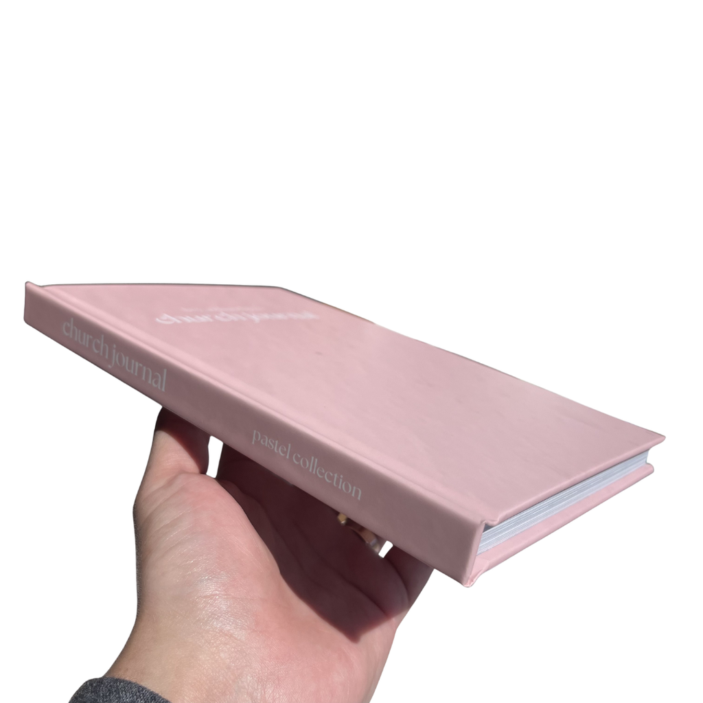Pink church journal held by a hand on a white background
